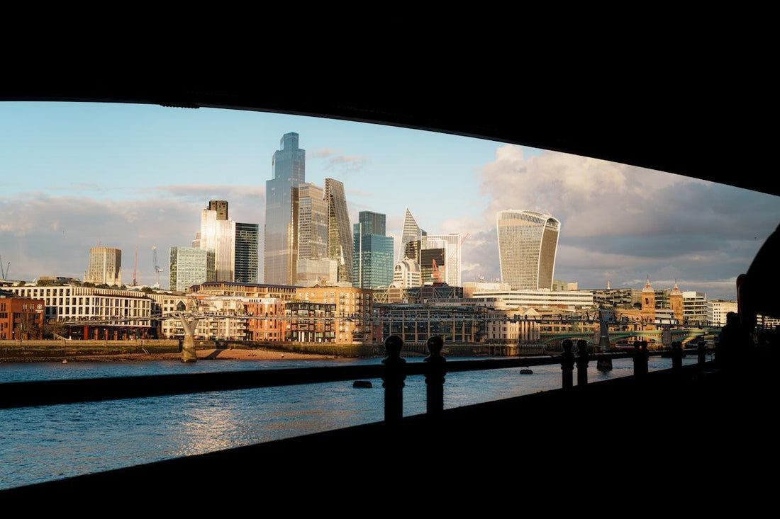 Modern city skyline with river and bridge in foreground.