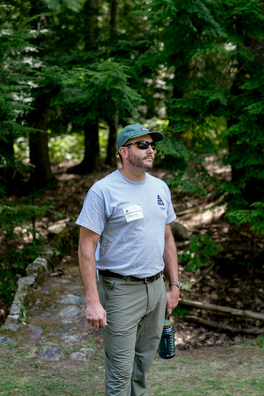 Man wearing a hat and sunglasses in a forest.