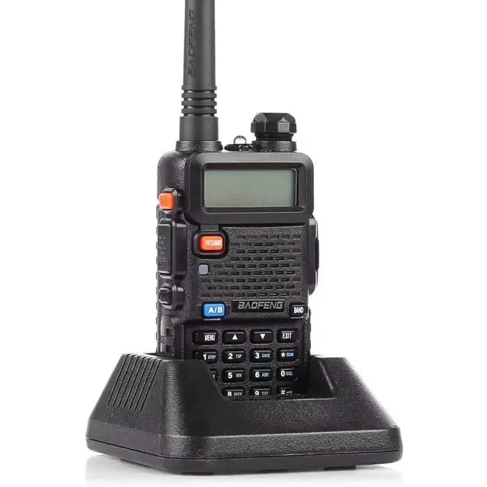 Black handheld two-way radio with an antenna, keypad, and LCD display, in a charging dock.