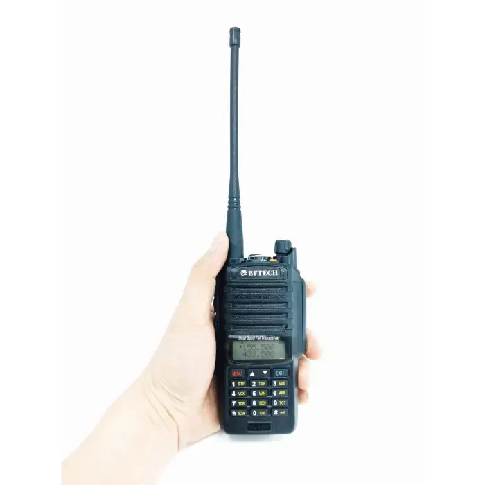 A black two-way radio with a long antenna and a numerical keypad, held in a hand.