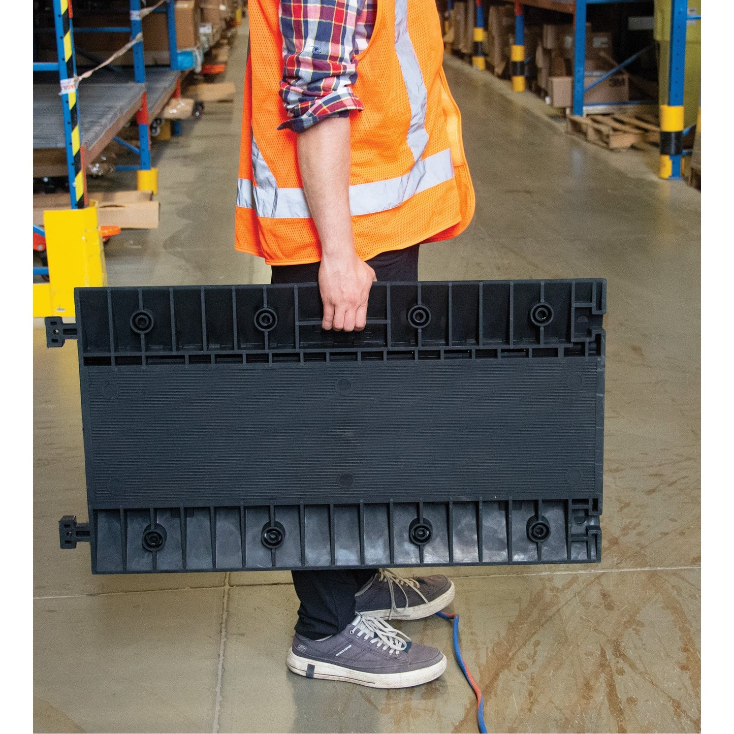 A person carrying a black, modular cable protector with multiple channels.