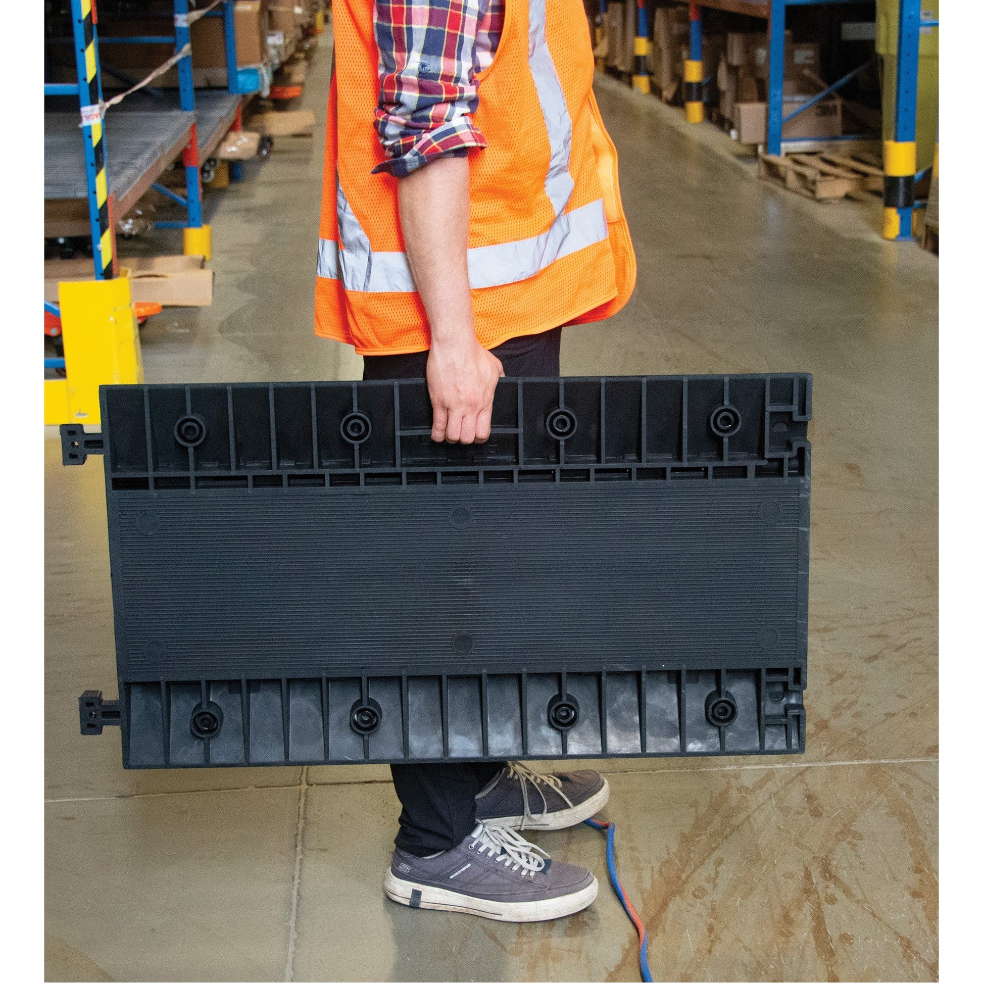 A person carrying a black, modular cable protector with multiple channels.